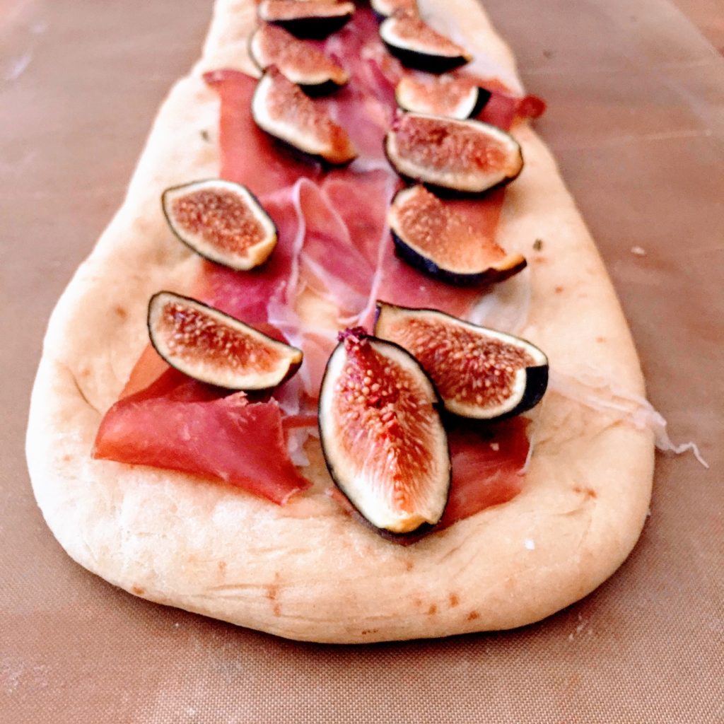 Pizza topped with sweet sliced prosciutto di Parma and wedges of fresh black seasonal figs