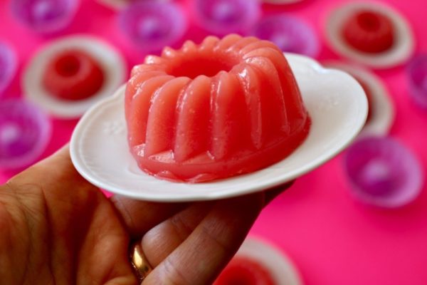 Pink watermelon pudding mono portions served on white porcelain dishes on a neon pink base with a jasmine flower on top sprinkled with cinnamon and chocolate