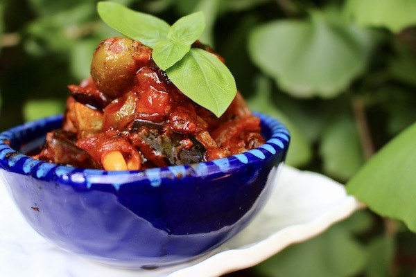 Baked eggplant caponata served on a blue bowl with basil