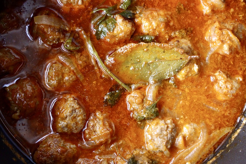 meatballs braised in a pot with broth, wine and bay leaves