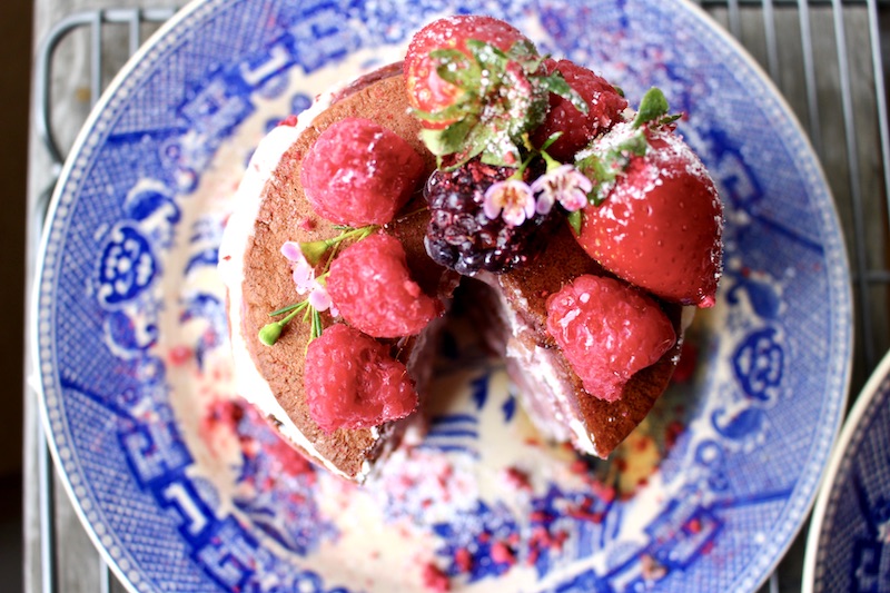 Pink pancakes stacked and filled with ricotta, covered with raspberries and blueberries and strawberries.Sprinkled with powder sugar and maple syrup.
