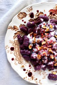 Decorate dish with purple sweet potato gnocchi topped with goat cheese sauce and hazelnuts