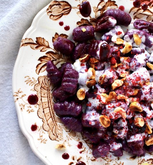 Decorate dish with purple sweet potato gnocchi topped with goat cheese sauce and hazelnuts