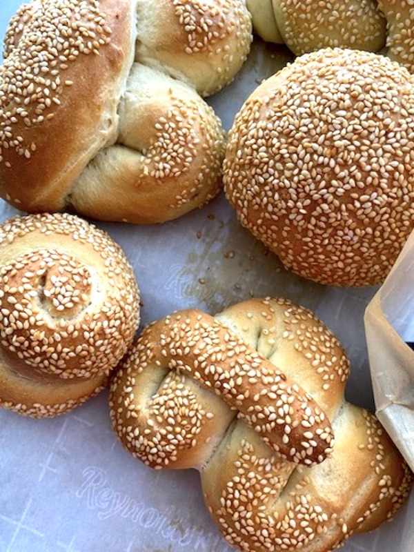 a basket with a white napkin filled with Sicilian bread buns, golden brown crust and sesame seeds on top