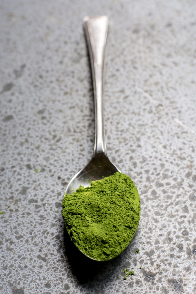 green tea powder in a spoon over a grey countertop